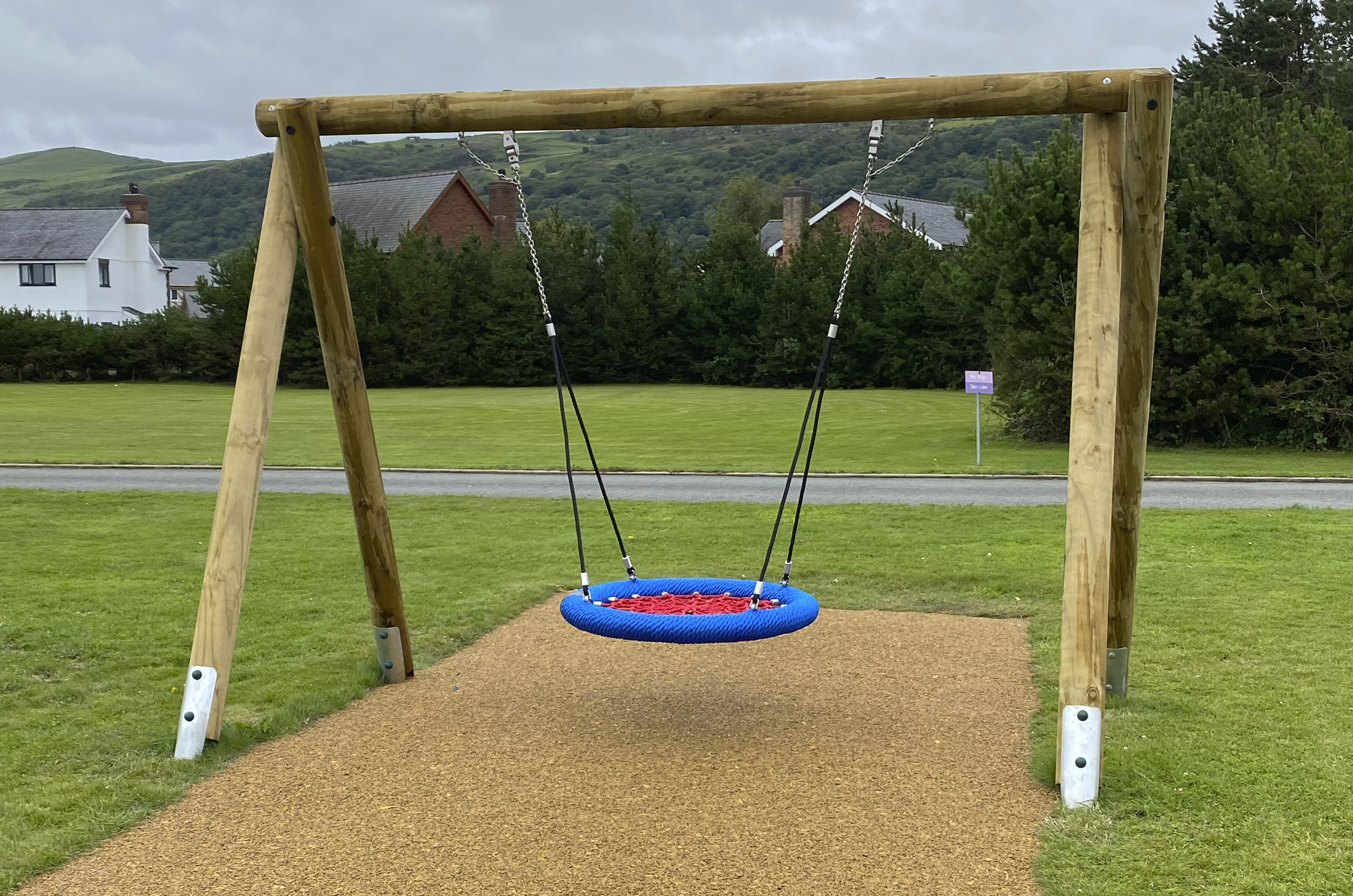 Timber Basket Swing - a timber swing frame holds a red and blue inclusive group basket with red ropes