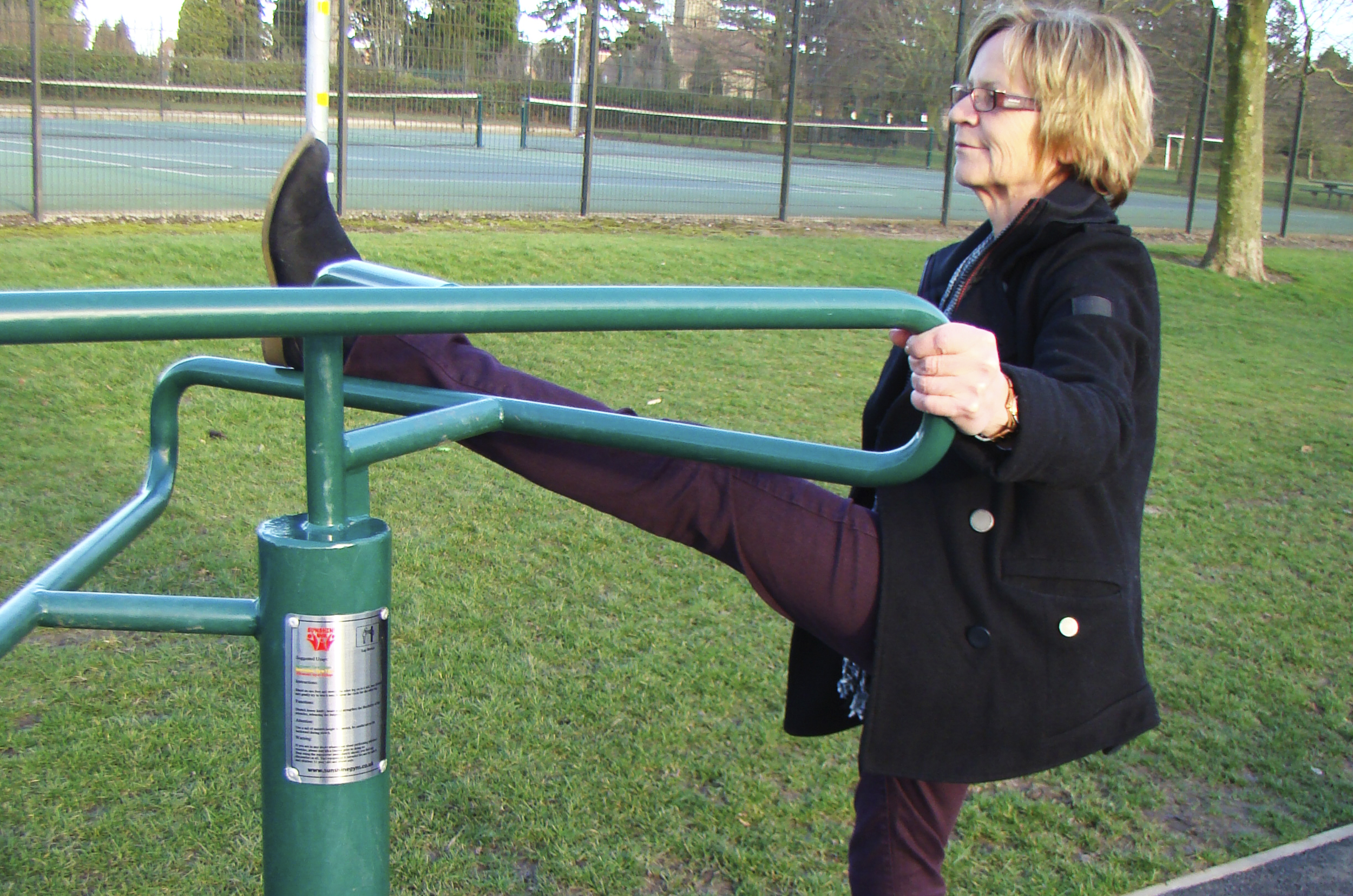 a lady stretches her leg up to the metal frame whilst holding on to another pat of the leg stretch