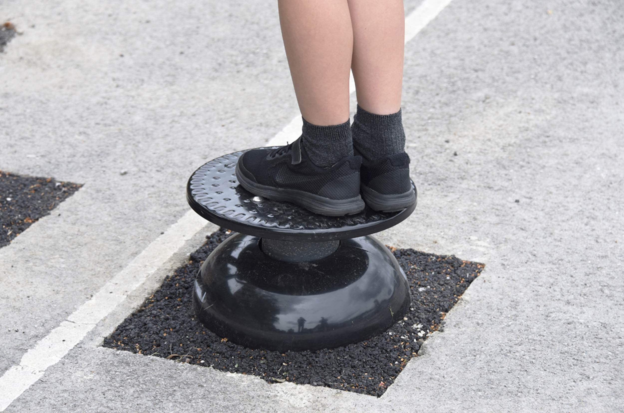A Childs feet stand upon a black circular disc sat on tarmac