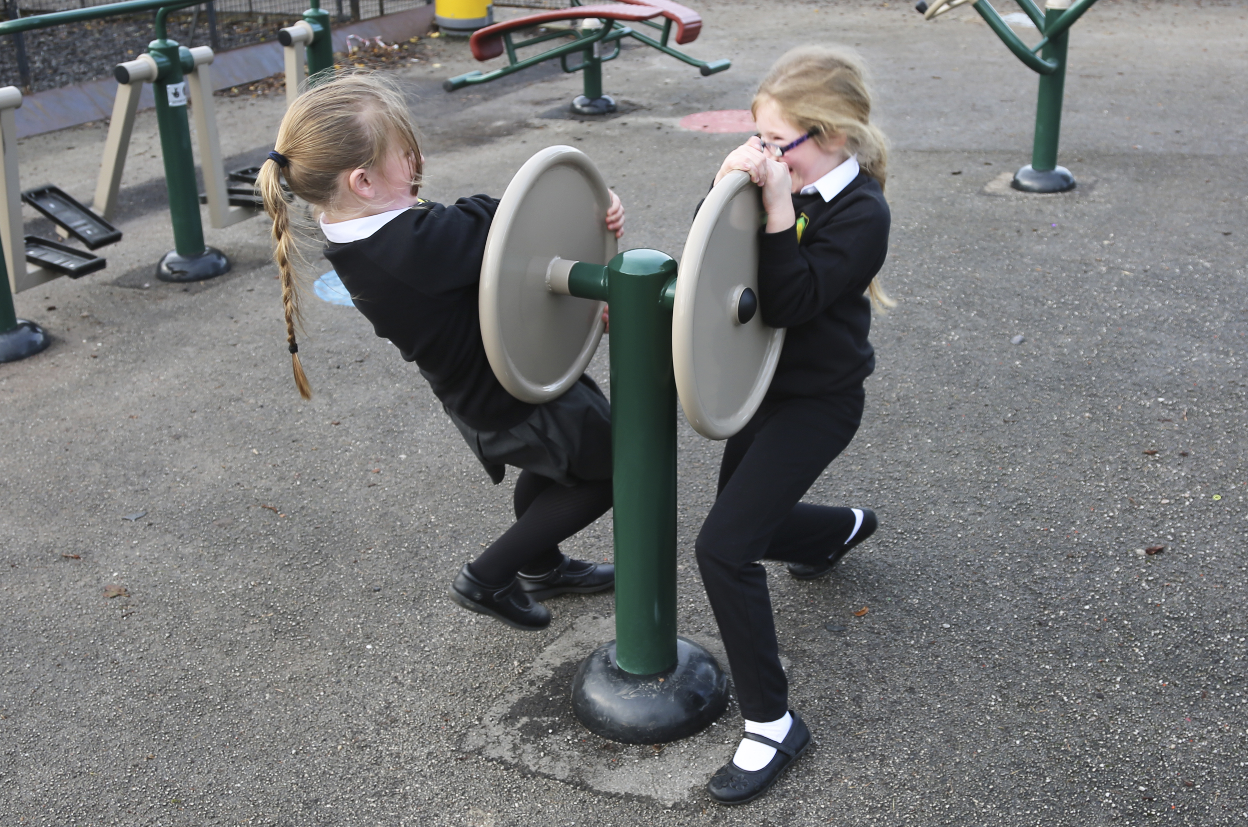 two girls use their strength to pull at a double disc held up by a single green post