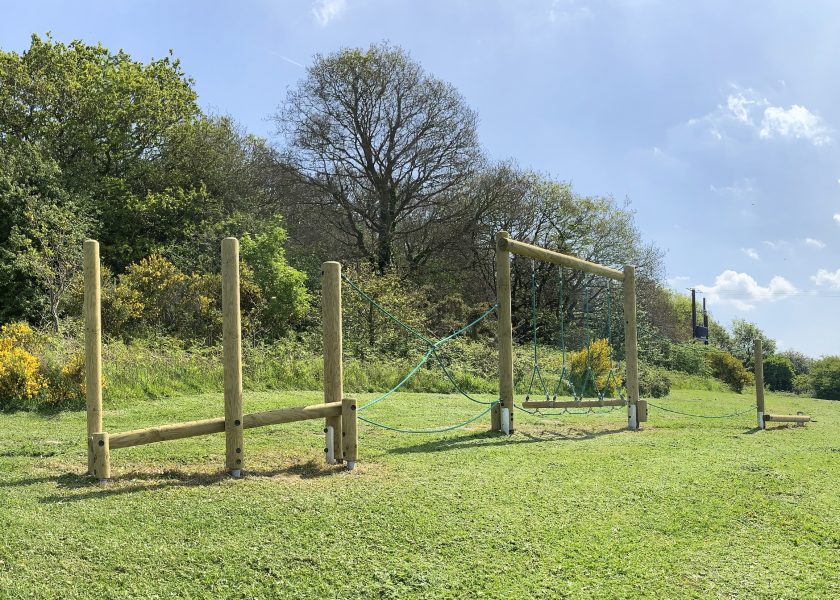 A series of vertical and horizontal timber complete with green ropes create an adventure trail, sitting on green grass with trees in the background