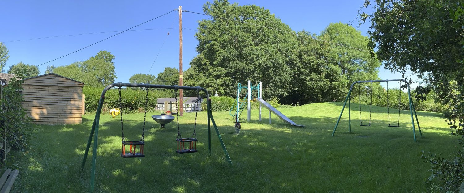 wistanstow play equipment swings, slide, spring riders and spinning dish installed in grass with trees in the background