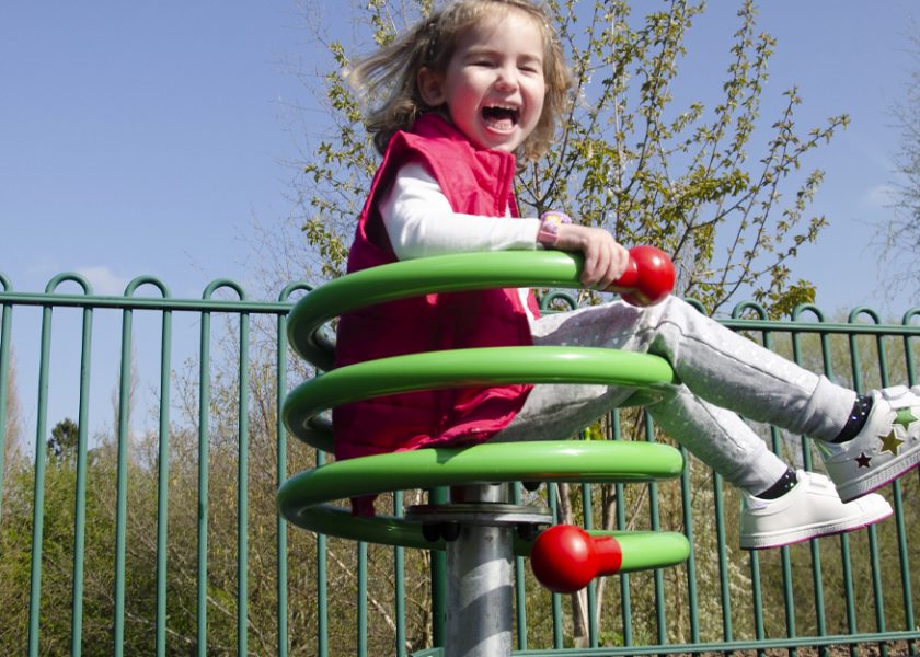 A young girl sits laughing as she spins around on a green curlicue spinner