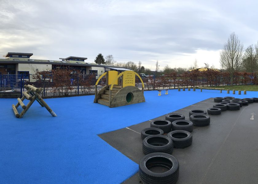 Old Park Nursery Blue Wetpour Safer Surfacing surrounded by tyres with A-frame Mini, Sleeper Tunnel with steps, Spring Wobble Plank, Steeping Logs and Balance Walk