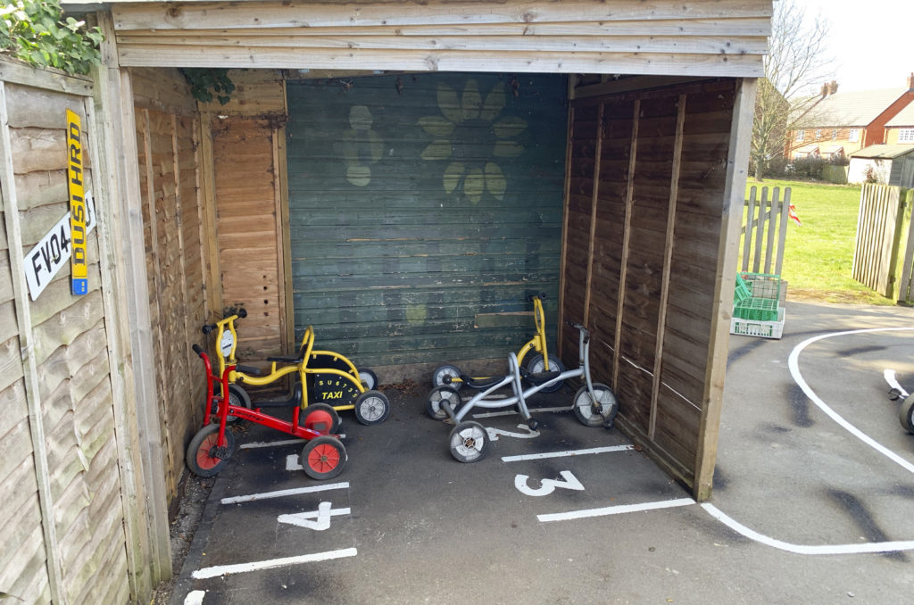 tricycles inside under cover with line marked numbered parking bays at Trinity CE Primary School