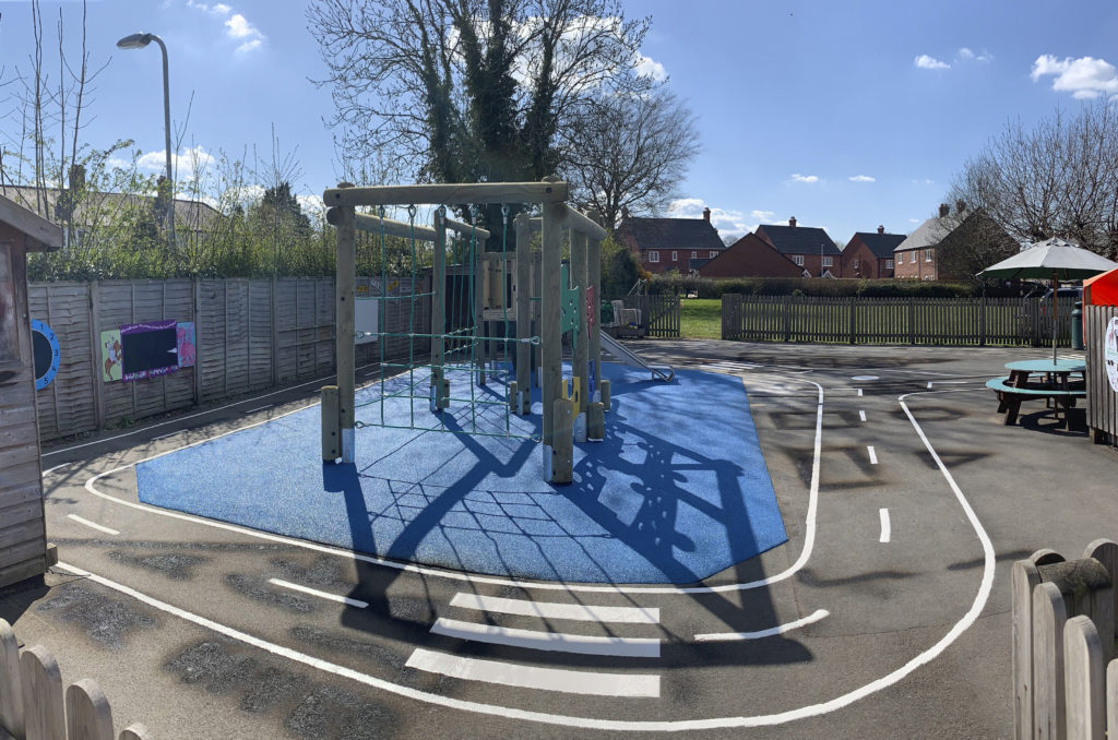 timber climbing frame with slide on blue wetpour safer surfacing surrounded by line marked roadway at Trinity CE Primary School
