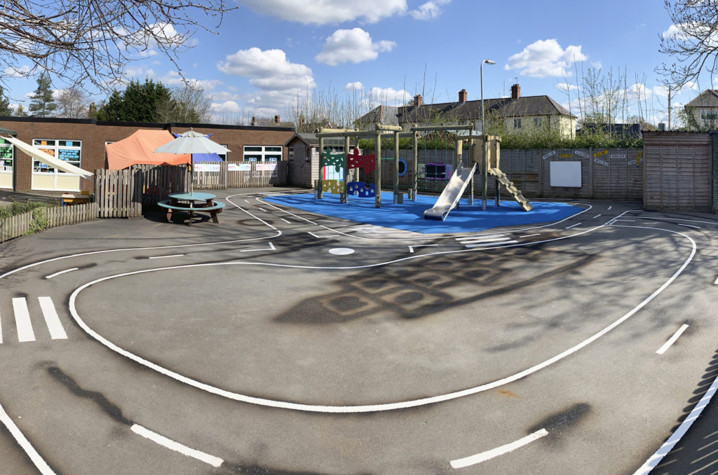 timber climbing frame with slide on blue wetpour safer surfacing surrounded by line marked roadway at Trinity CE Primary School