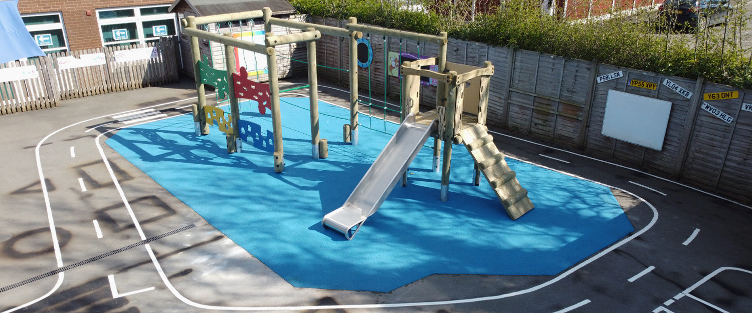 timber climbing frame with slide sit on blue wet pour surface at Trinity CE Primary School