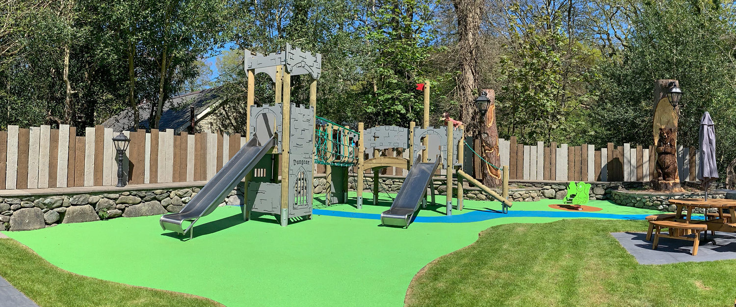 Ysgethin Inn Castle themed play equipment with two slides and dragon spring rider on green and blue wetpour safer surfacing