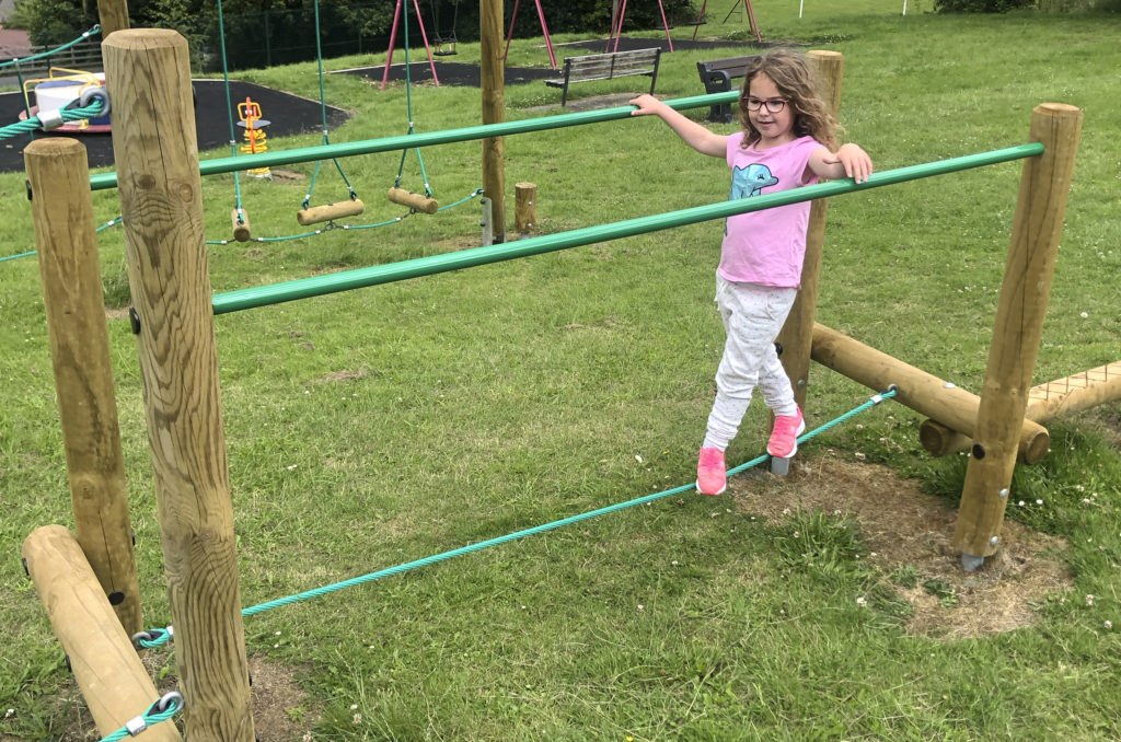 Adventure Trail at Bausley with Criggion, girl balances on a green rope whilst holding green hand rails