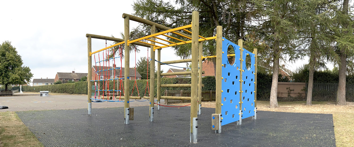 The Grange School Playfame - Timber post frame with yellow climbing ladders, red and blue netting and blue climb walls on black rubber grass mat safer surfacing with trees and hedges in the background