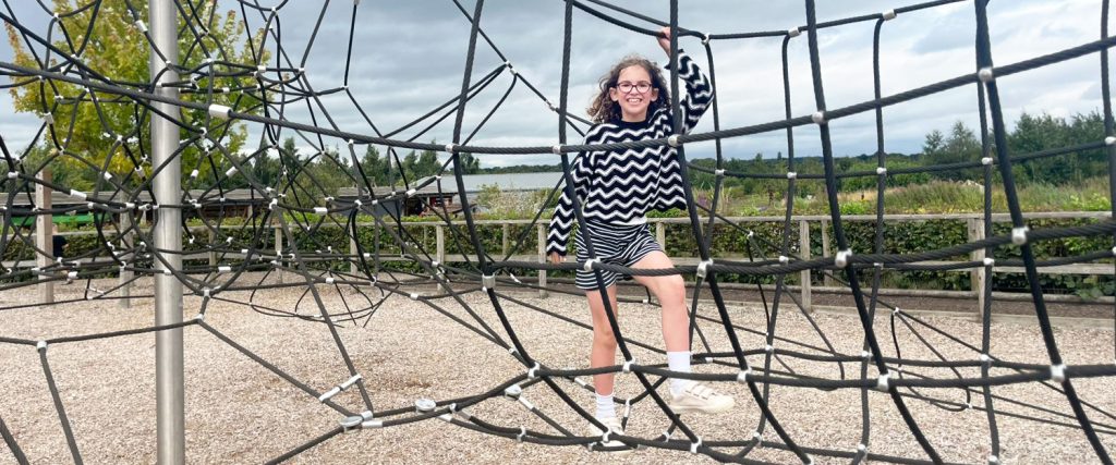 A young girl stands smiling on a black rope climbing net